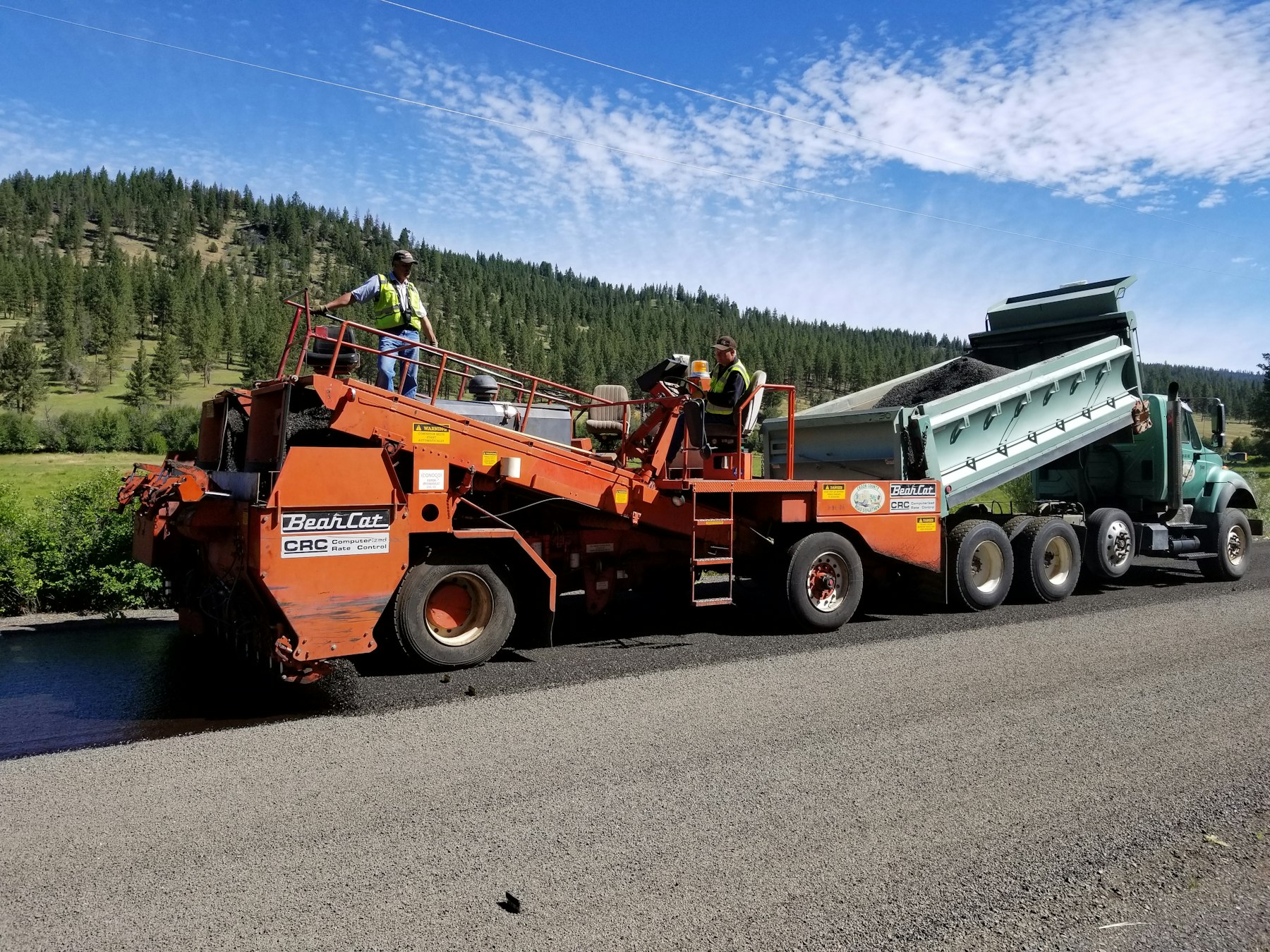 A paving machine and dump truck laying fresh asphalt on a road