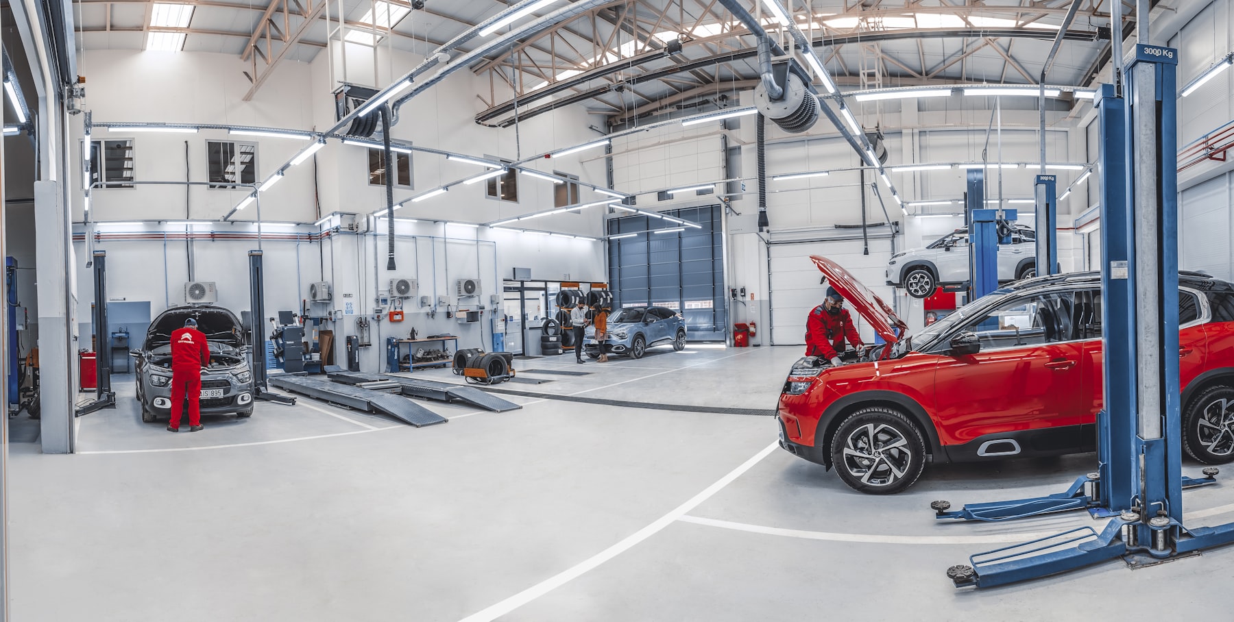 Two mechanics working on cars inside a bright, spacious auto repair shop