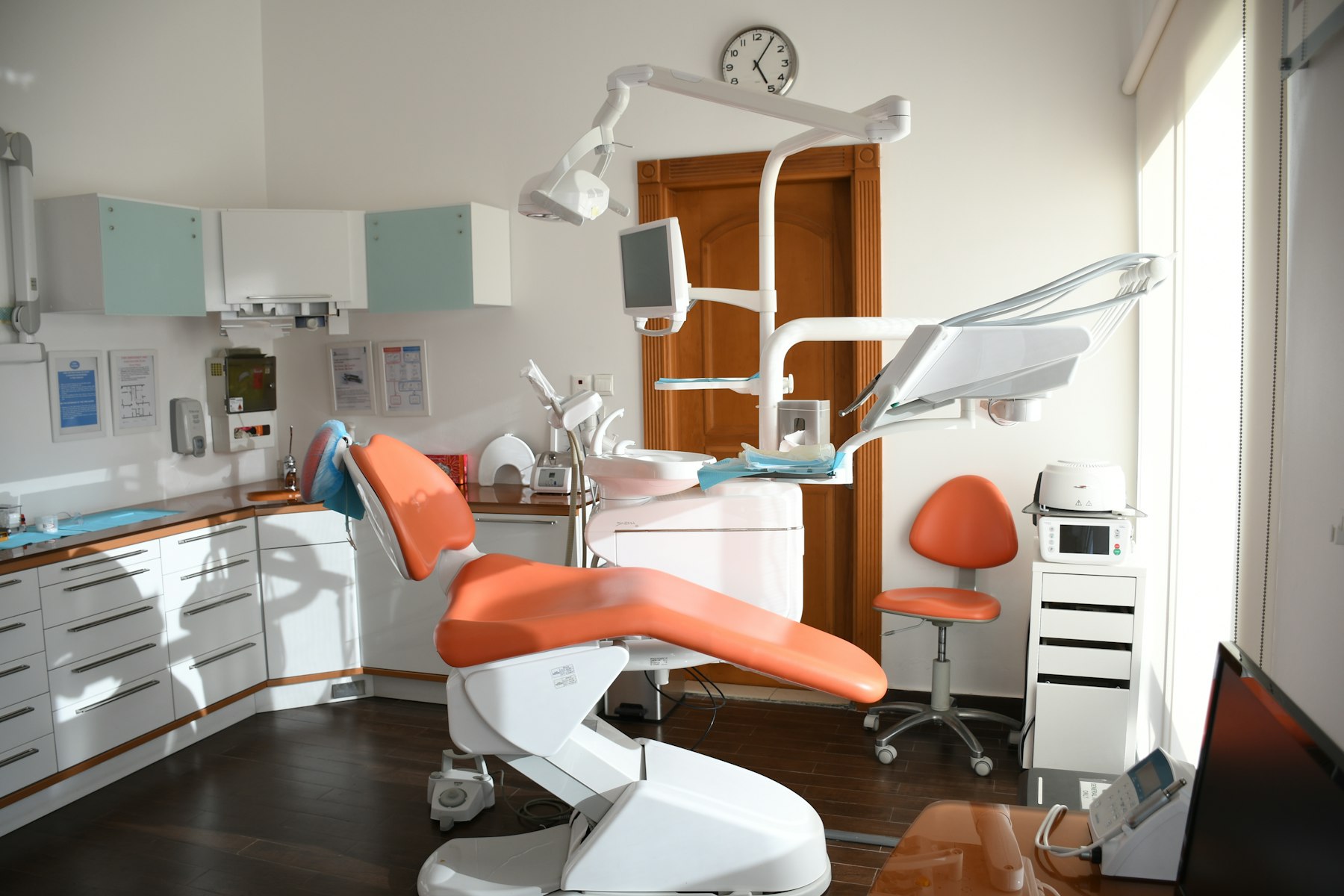 An orange dental chair with equipment in a bright clinical office