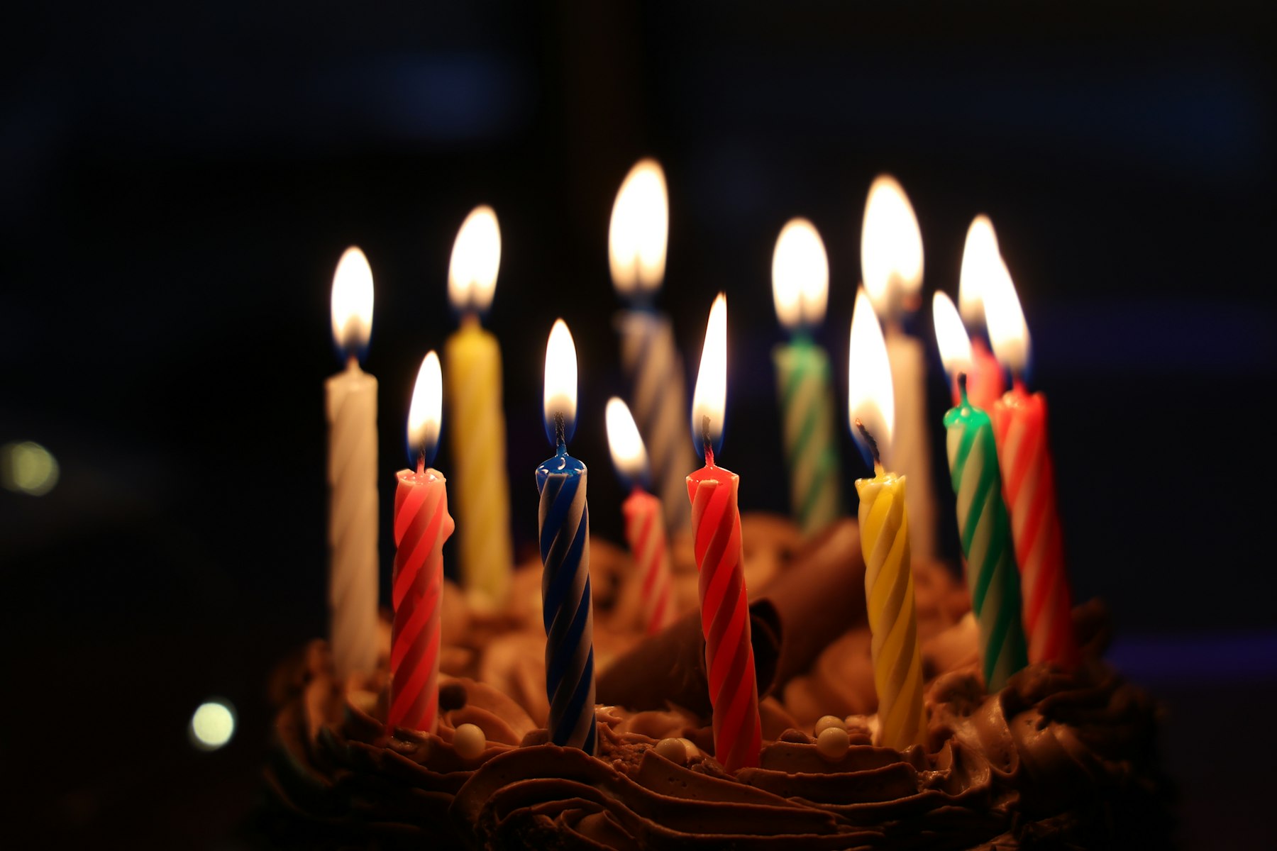 A chocolate birthday cake topped with many lit candles