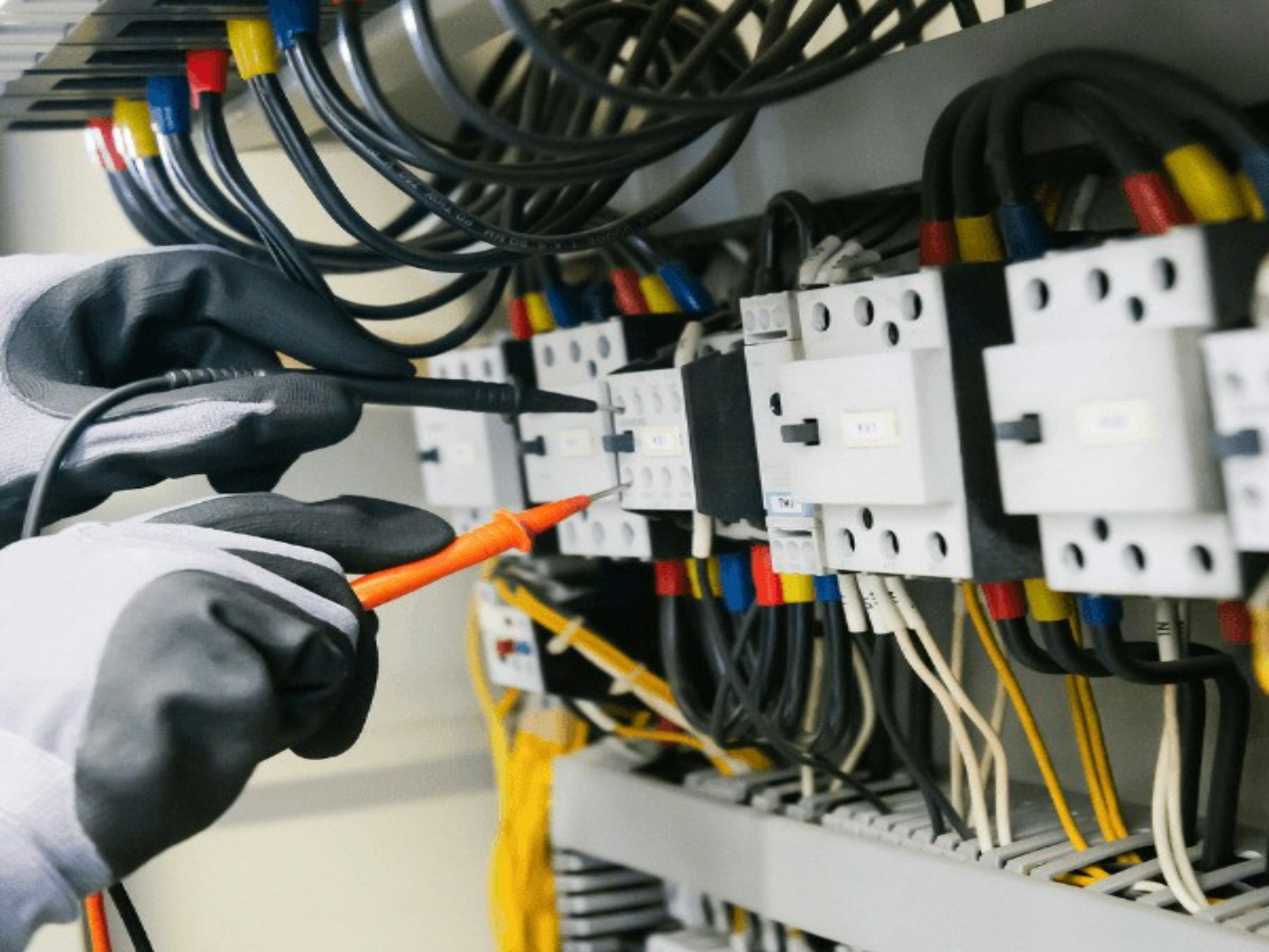Gloved hands testing an industrial electrical panel with a multimeter