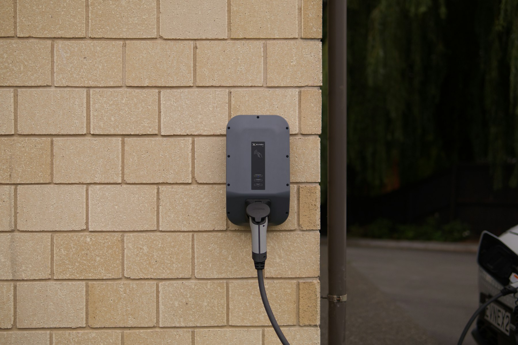 A wall-mounted EV charger with cable on a home garage exterior