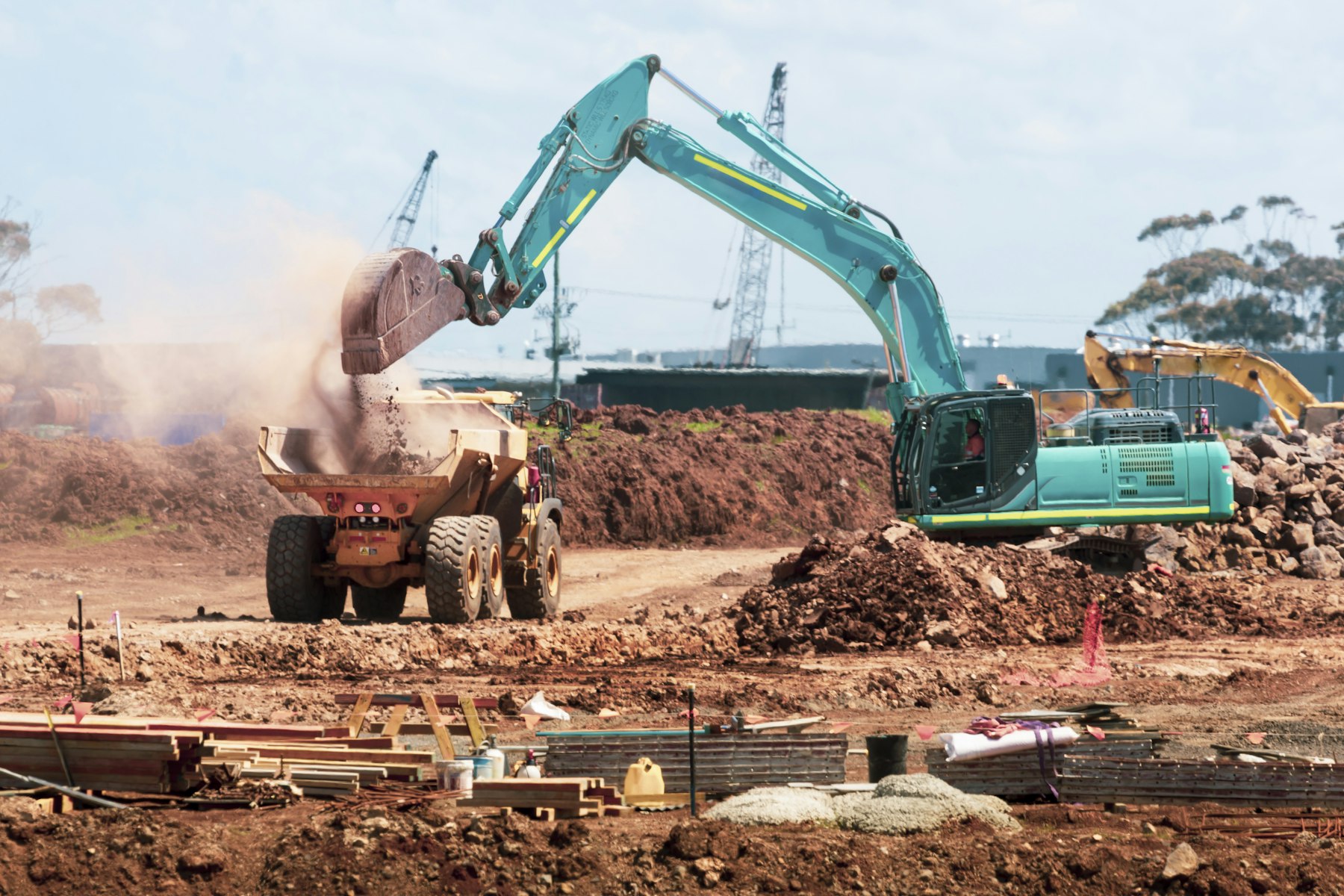 An excavator loading soil into a dump truck at a graded construction site