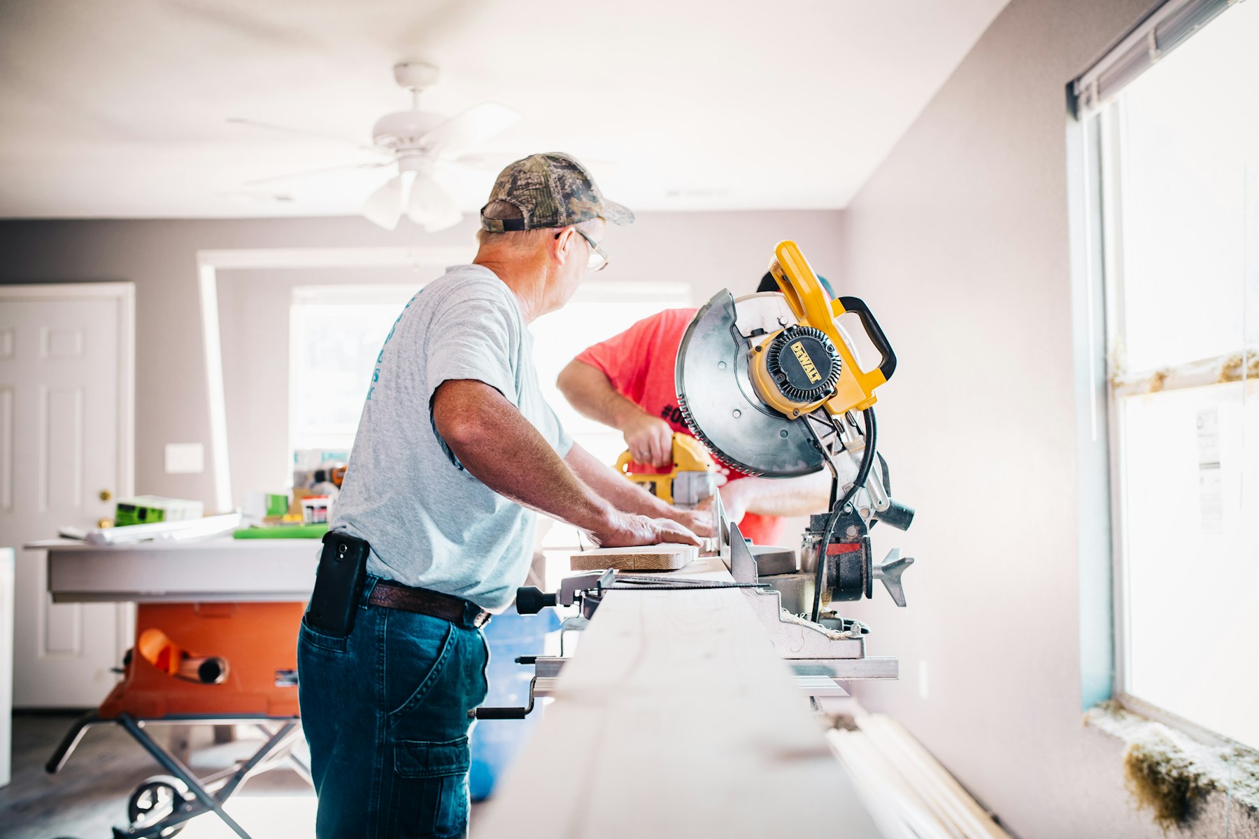 Two carpenters cutting trim on a miter saw inside an unfinished room