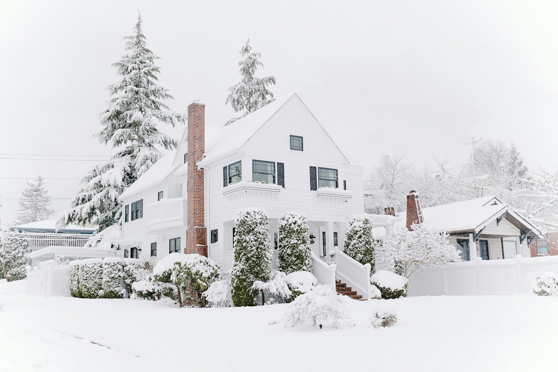 A snow-covered two-story house with a brick chimney in winter