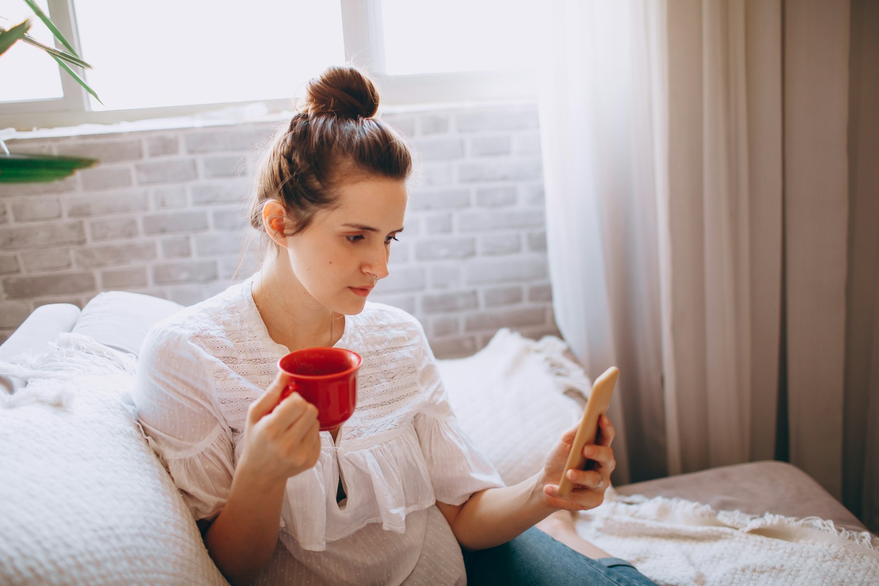 A woman drinking coffee while scrolling a feed on her phone in the morning