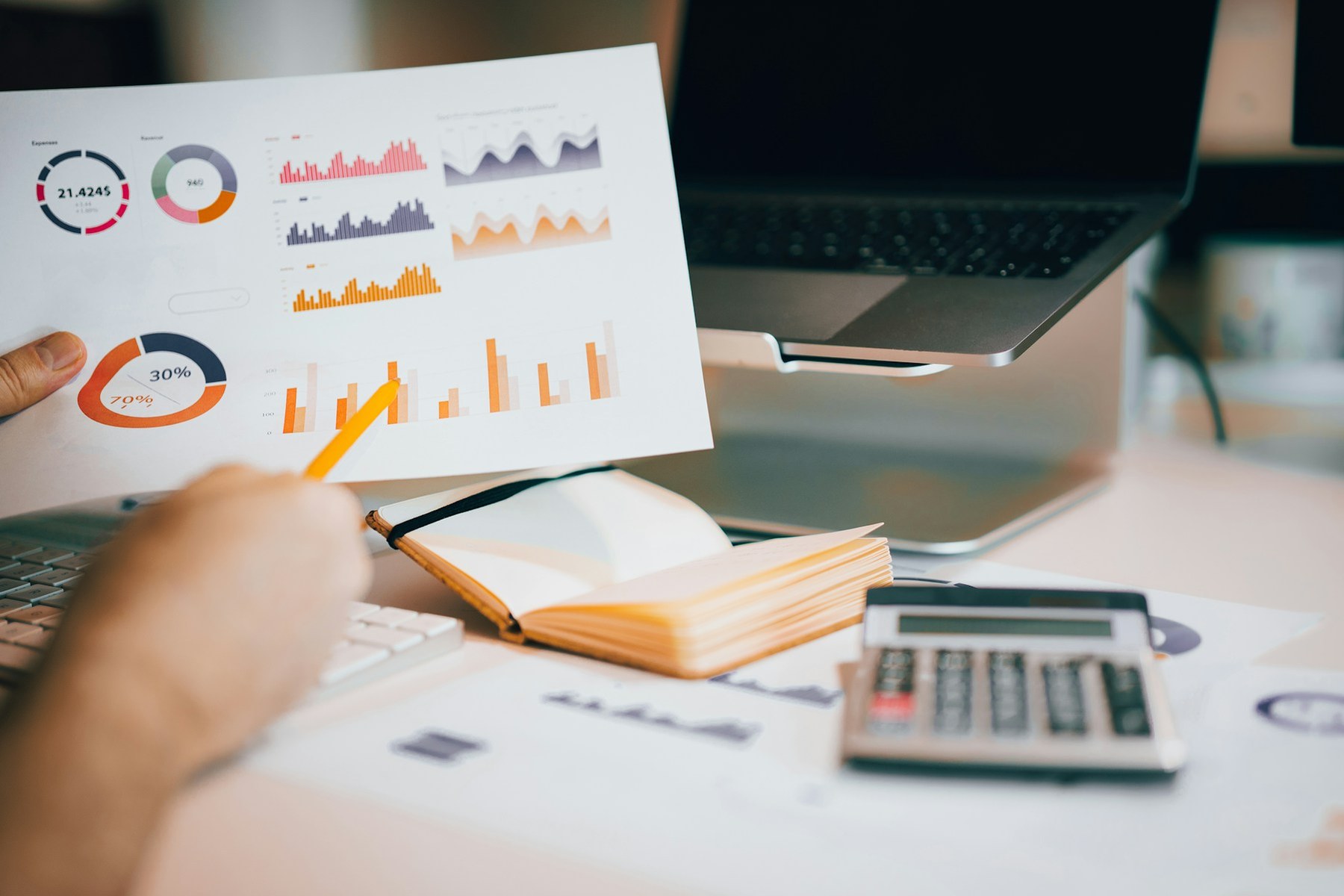 Printed charts and a calculator beside a laptop on a desk