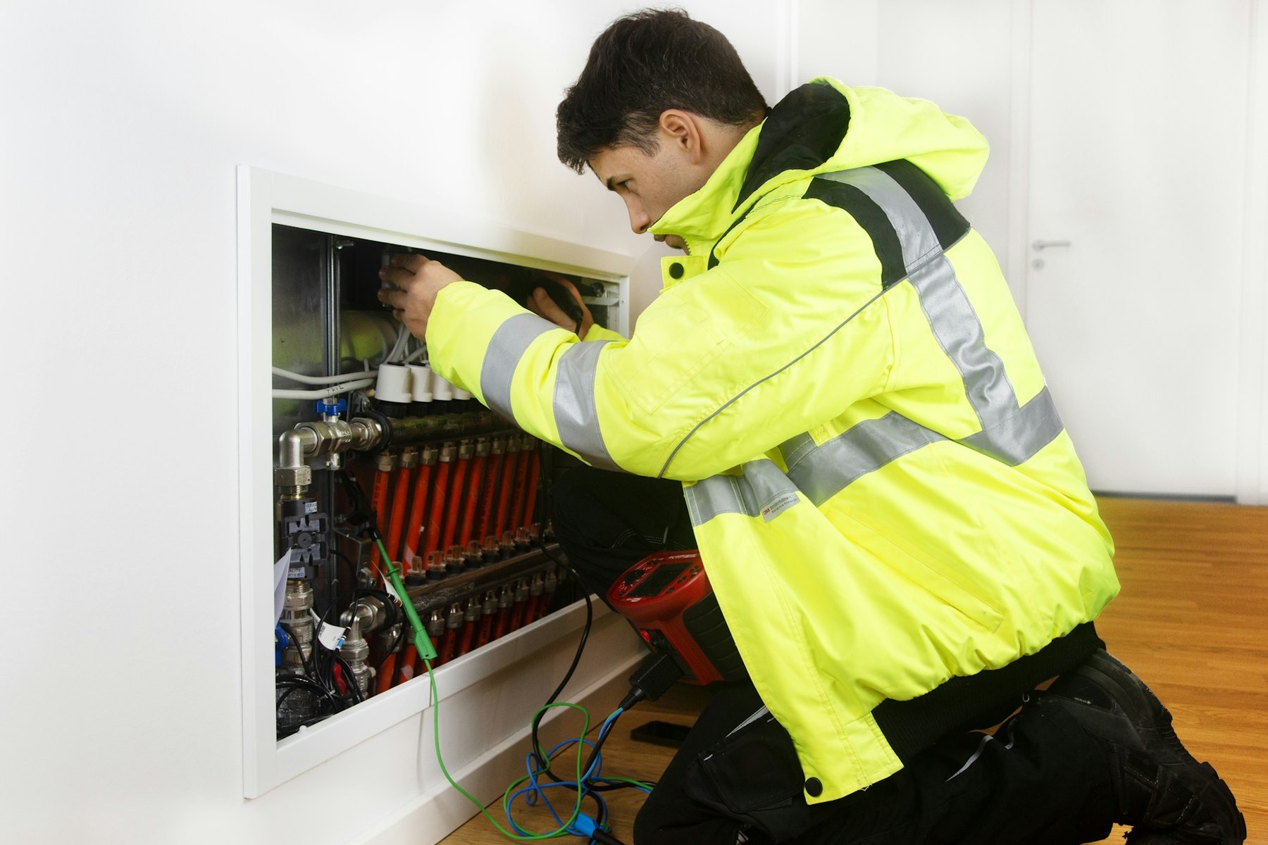 A technician in a hi-vis jacket working on wall-mounted equipment