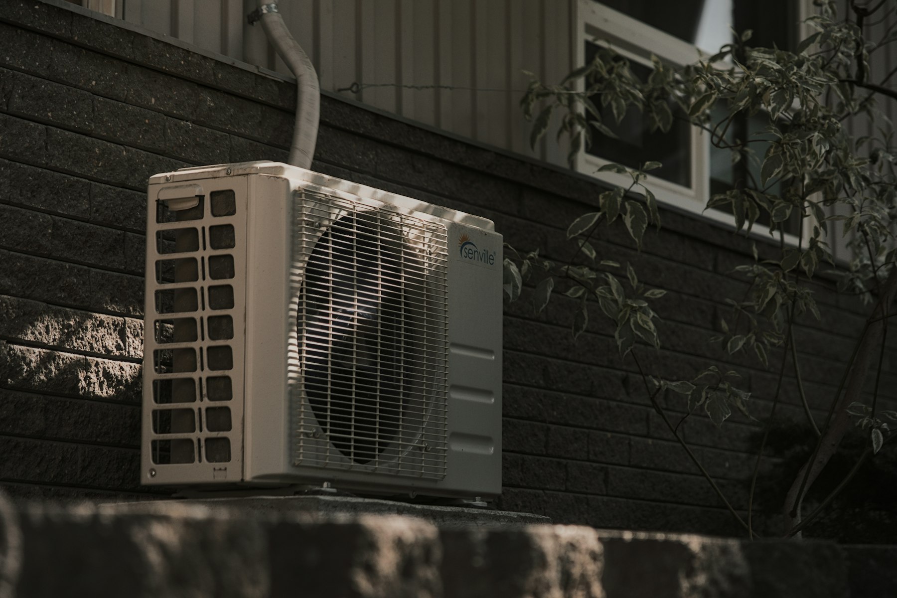 A residential air conditioning condenser unit mounted against a brick wall