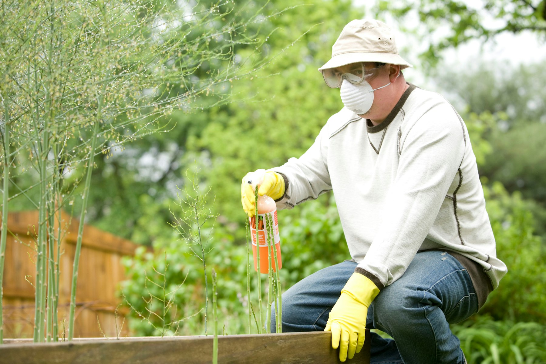 A worker in protective gear, respirator, and yellow gloves applying pest treatment outdoors