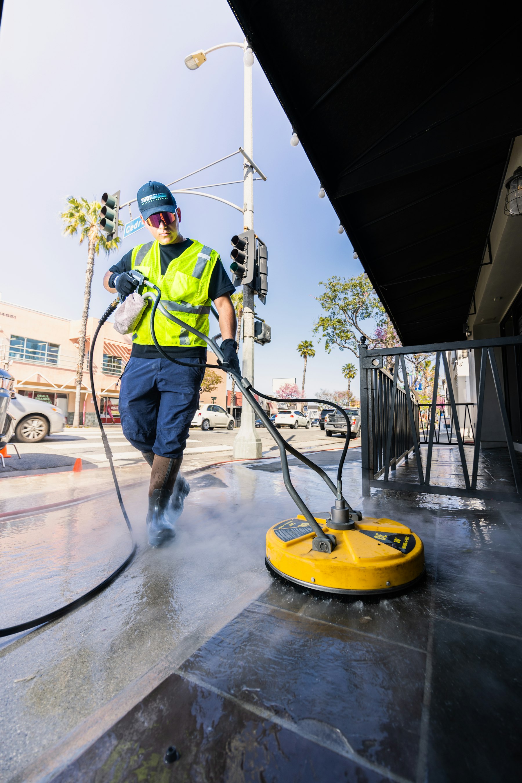 A worker in a yellow vest pressure washing a paved surface