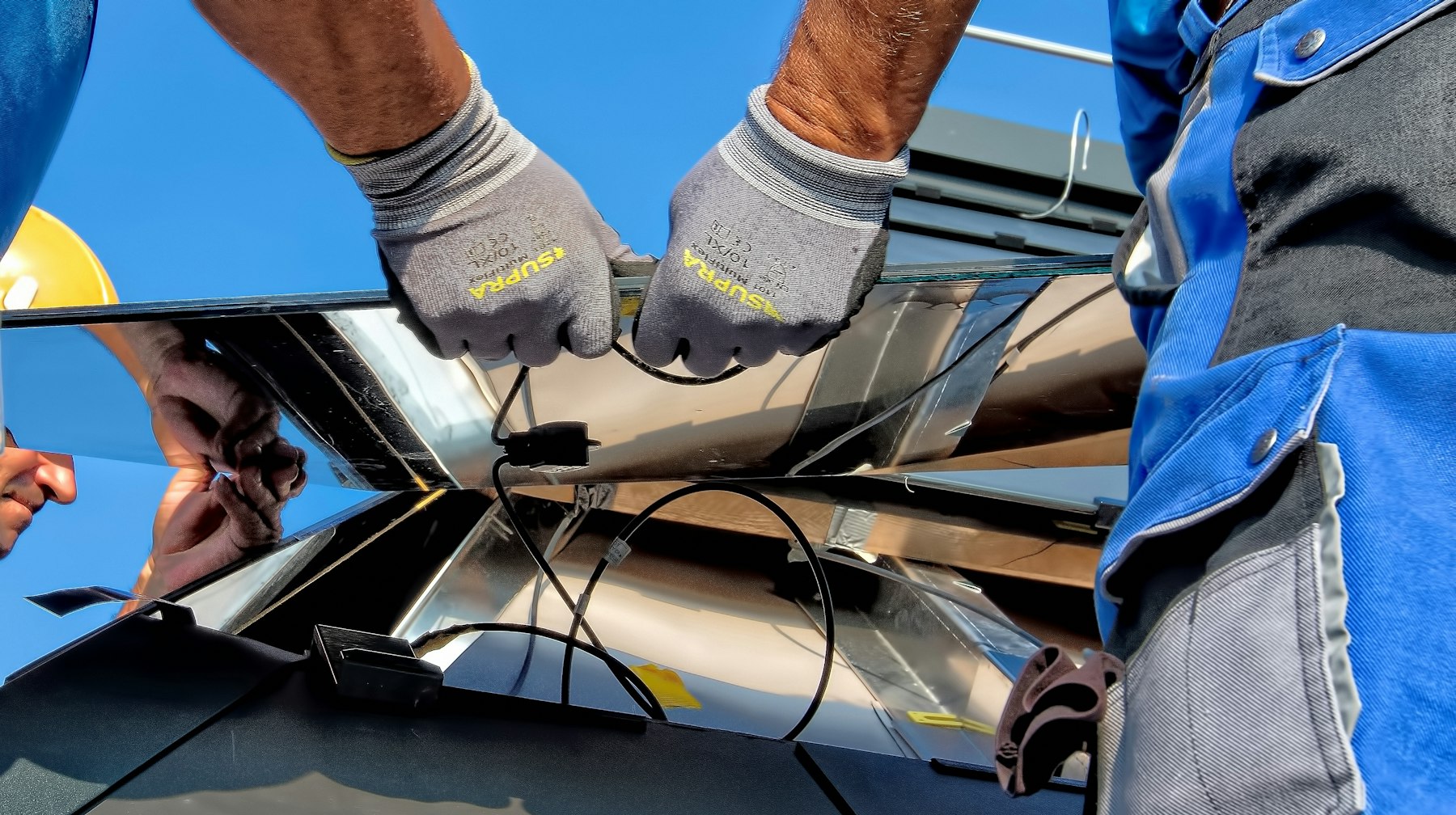 An installer's gloved hands working on a solar panel connection