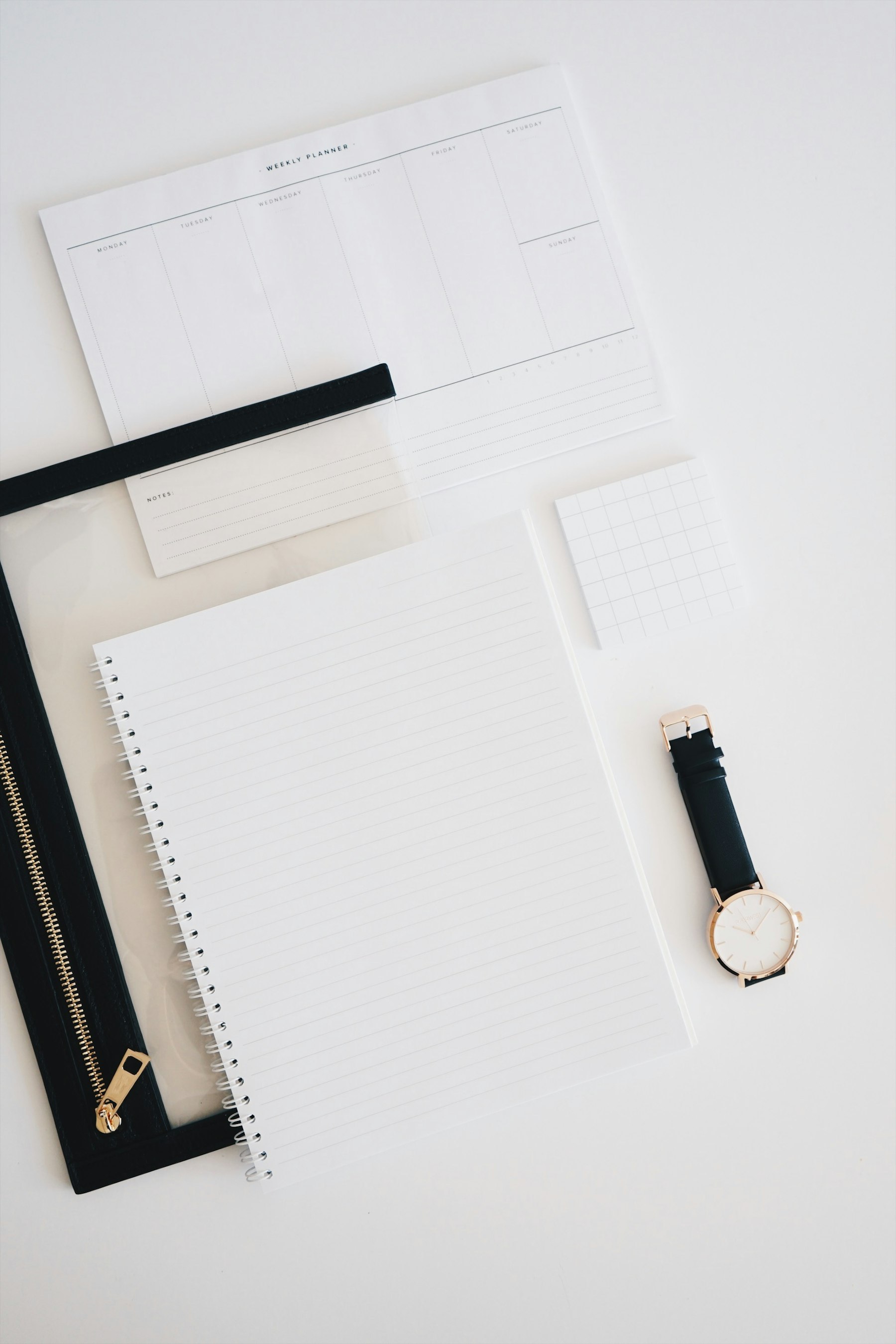 A wristwatch resting on a desk beside an open notepad and planner