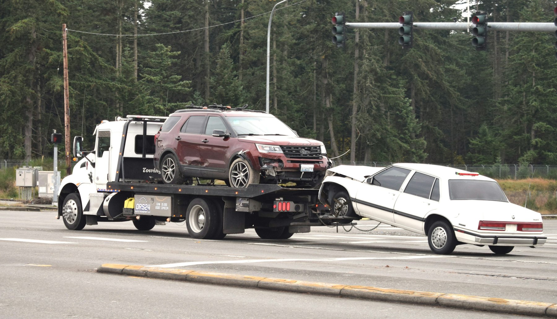 A flatbed tow truck hauling a damaged vehicle through an intersection