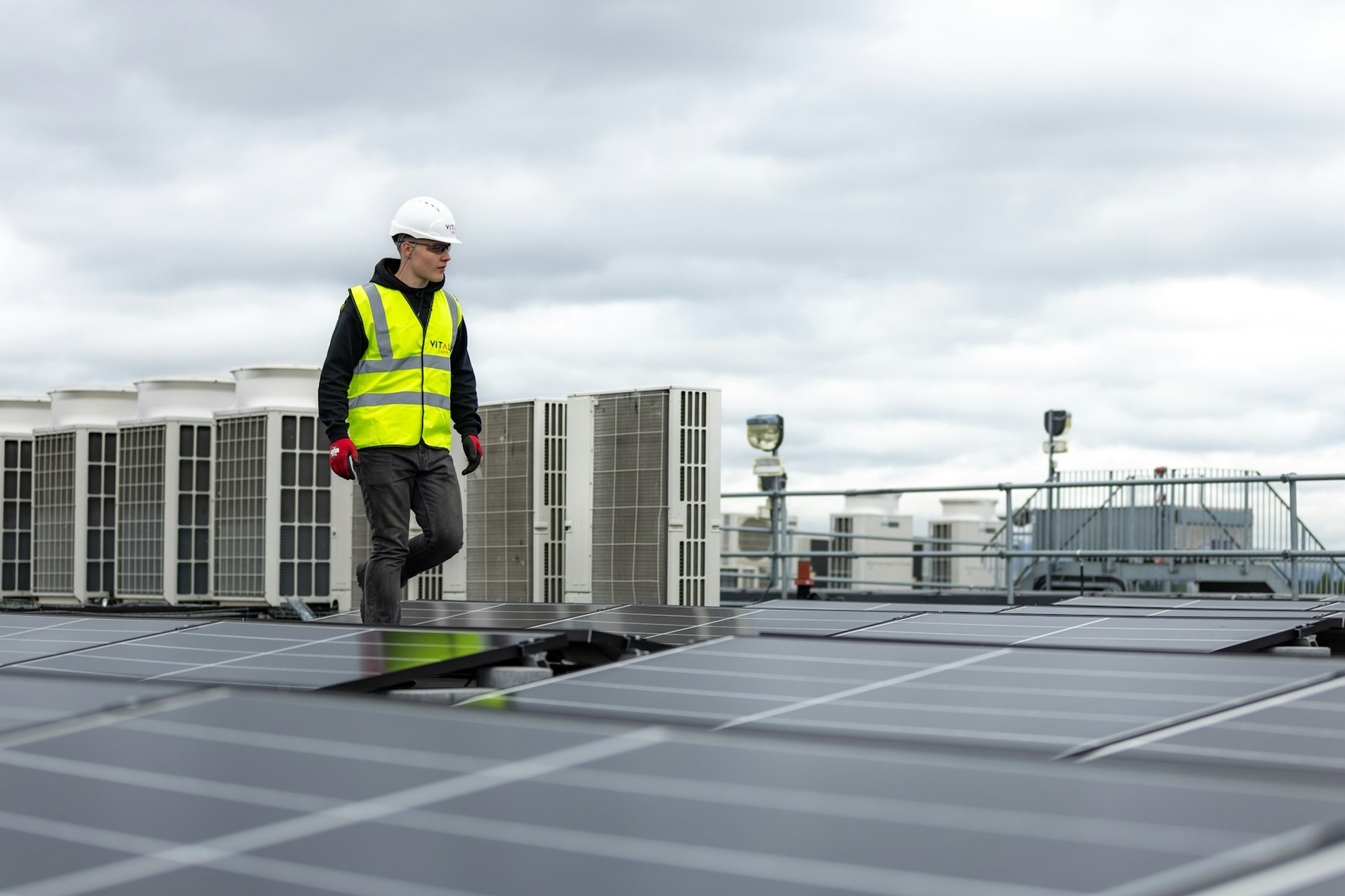 A worker in a hi-vis vest walking past rooftop HVAC condenser units