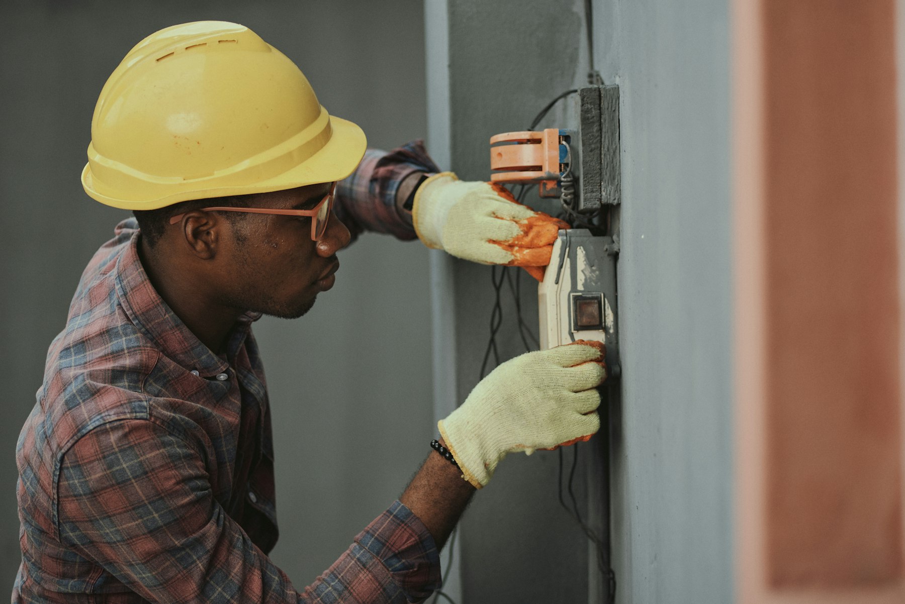 An electrician in a hard hat and work gloves wiring an electrical panel