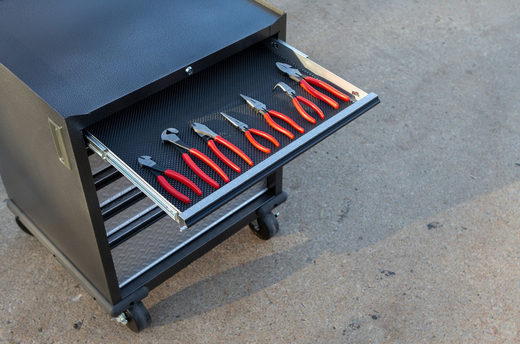 A rolling mechanic's tool cart with a drawer of pliers open