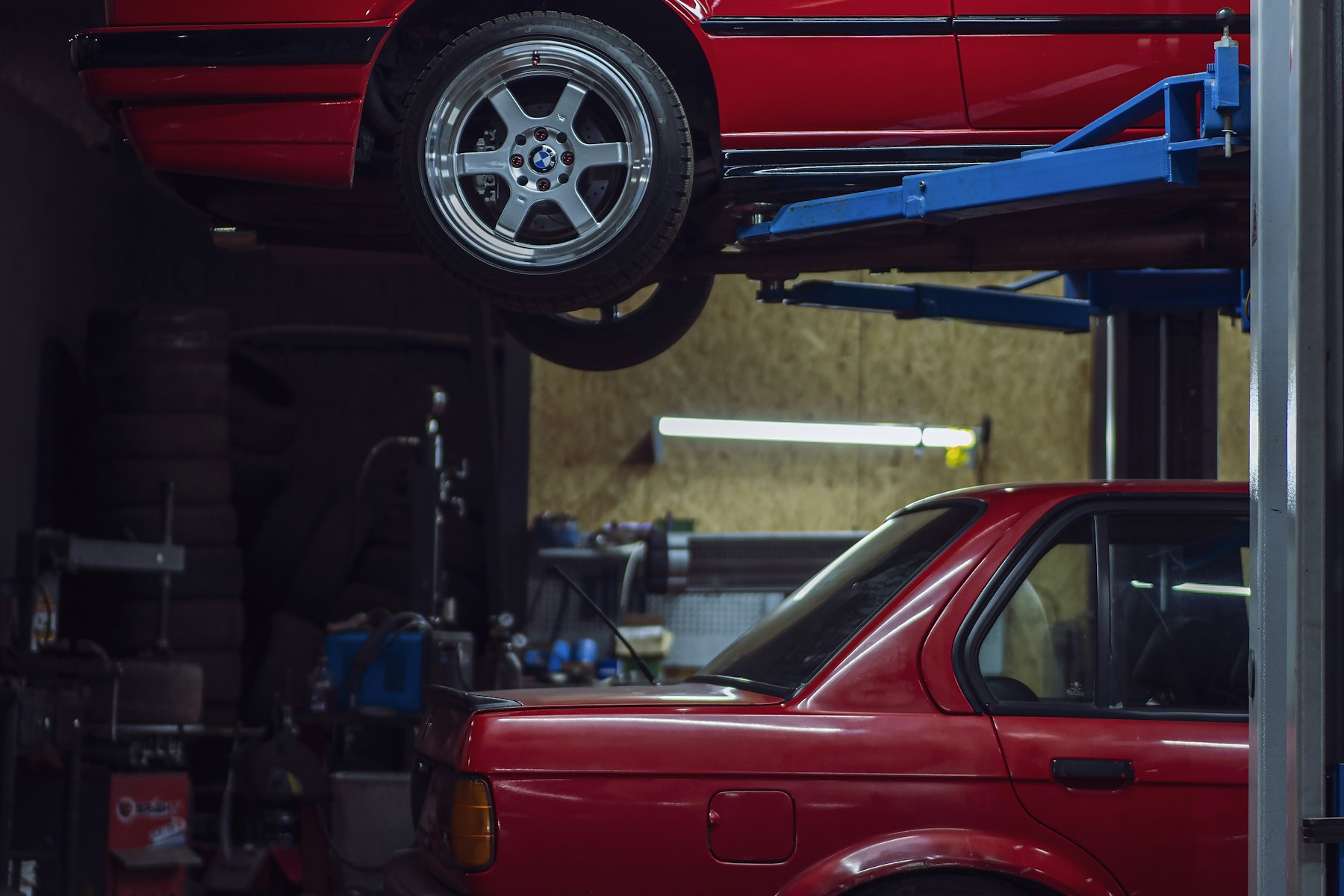 Two cars in a repair garage, one lifted on a two-post lift