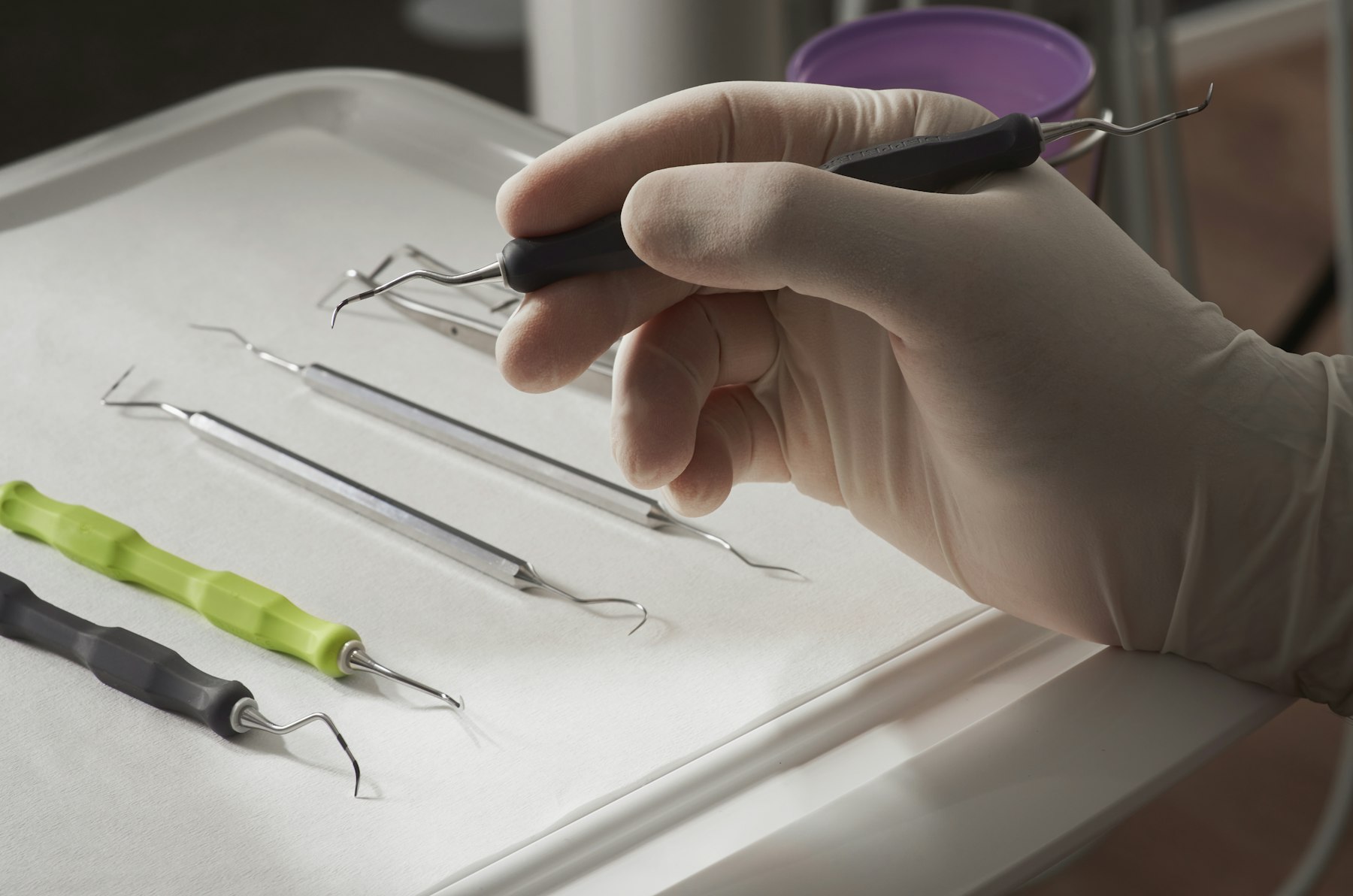 A gloved hand picking up dental instruments from a tray