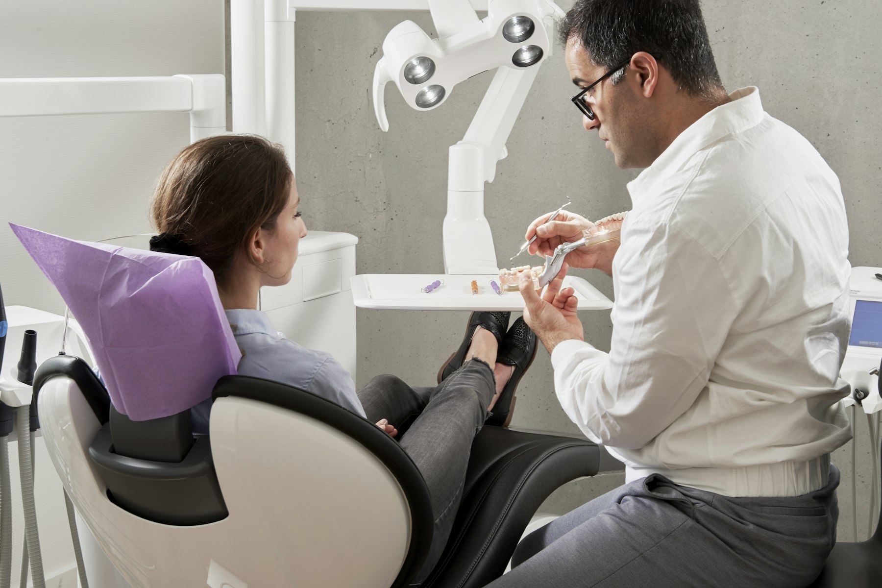 A dentist reviewing a dental model with a seated patient in a modern clinic