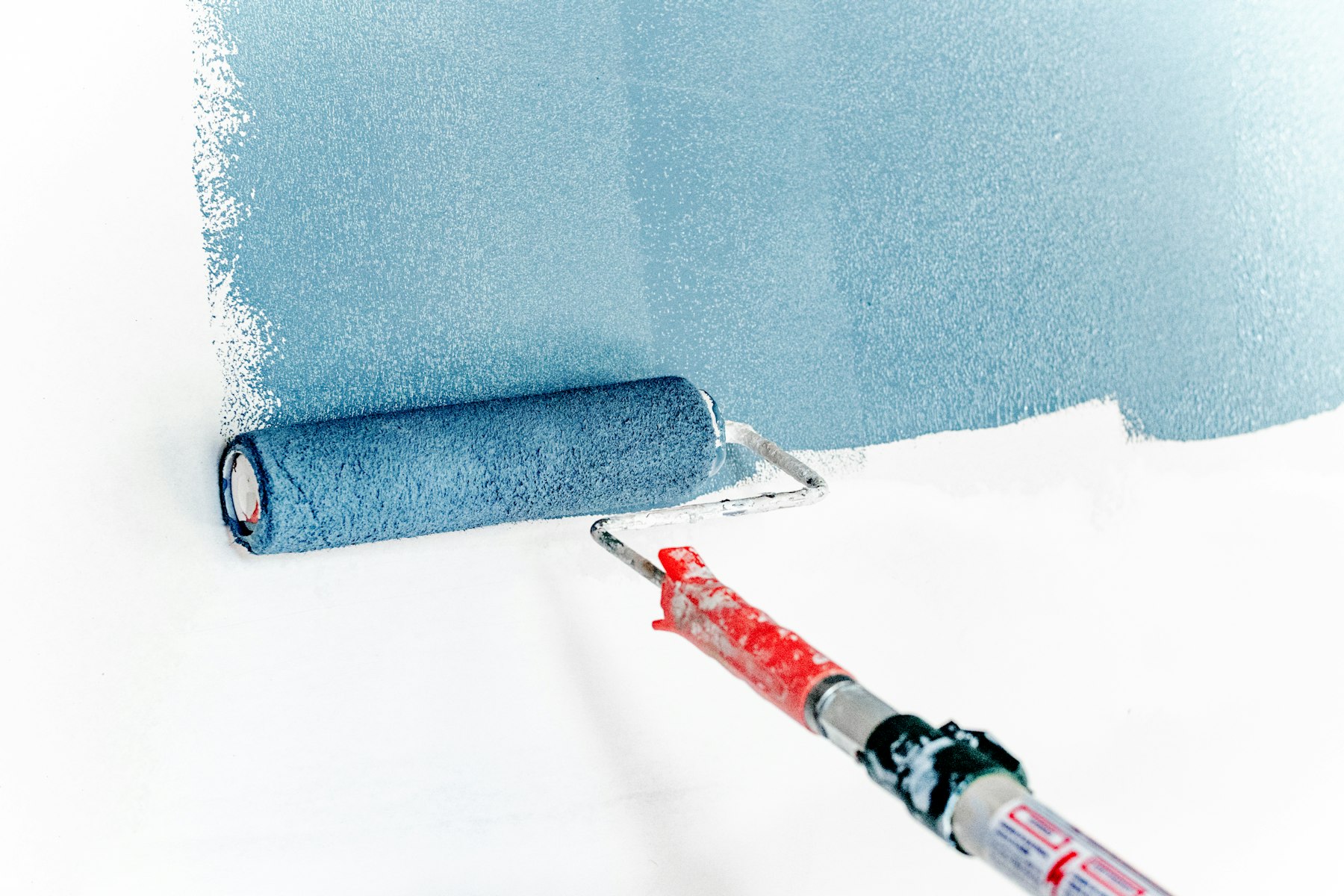 A paint roller applying blue-gray paint to a white wall
