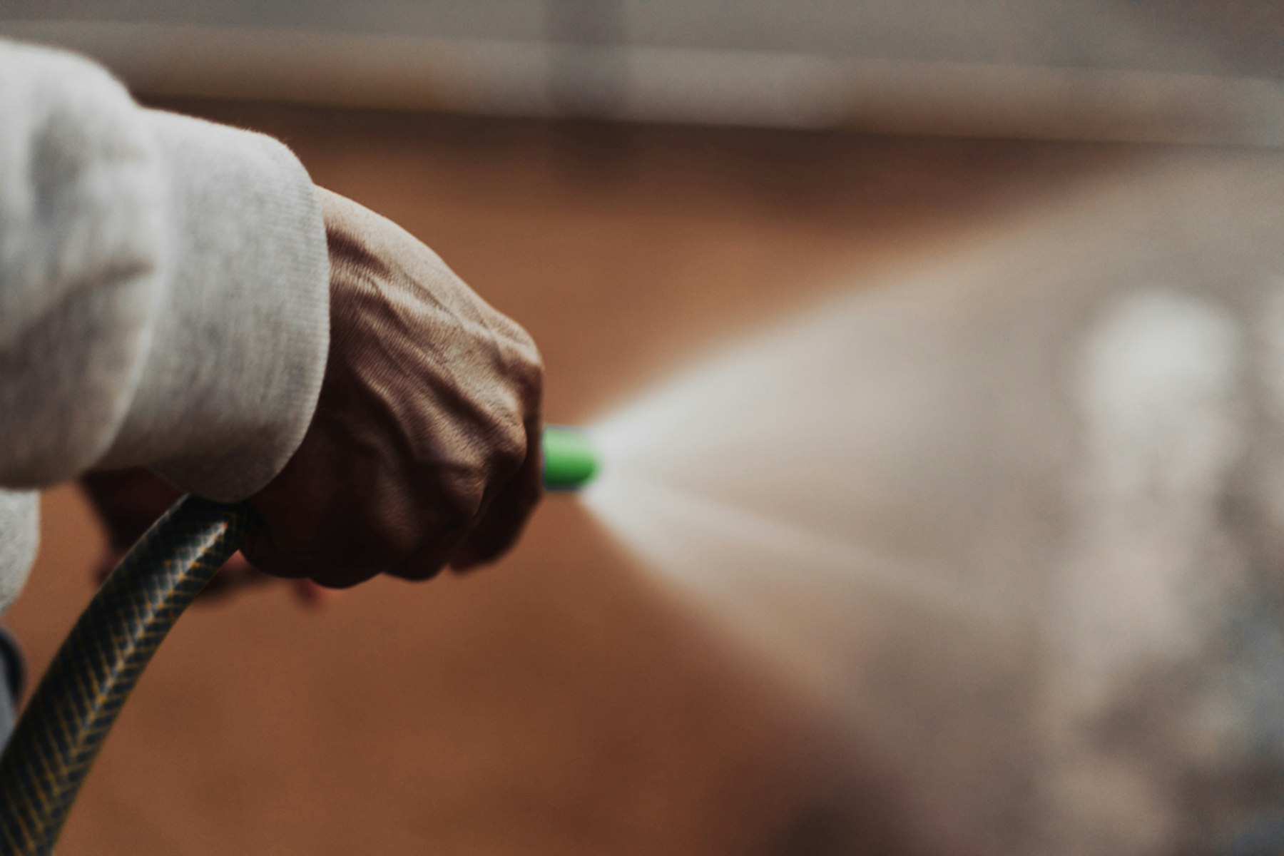 A hand aiming a spray applicator, treatment mist visible in the air