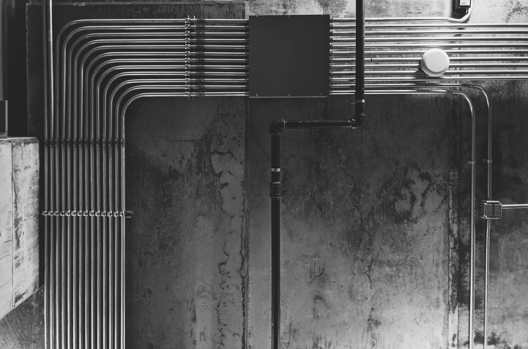 Overhead industrial pipework mounted against a concrete wall